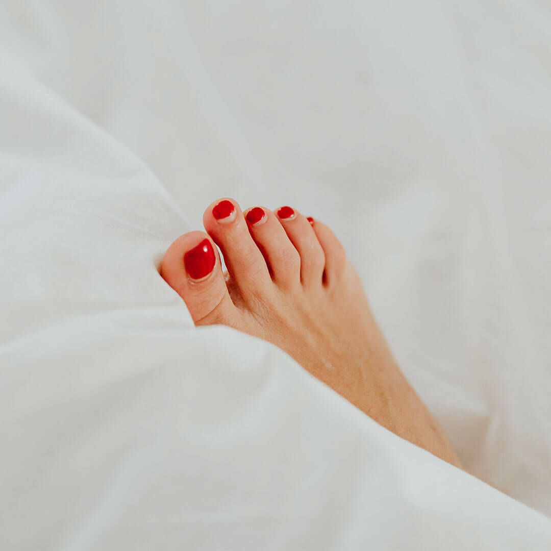 A woman's foot with red painted toenails on a bed.